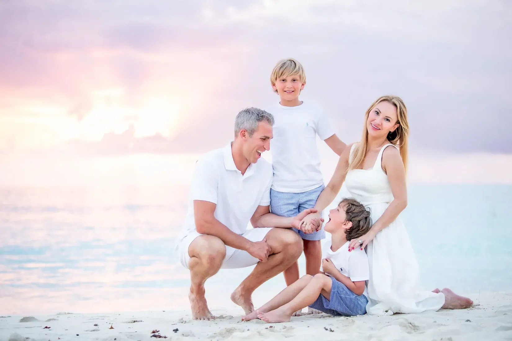 Parents and two young boys posed together on the sand at sunset in Grand Cayman