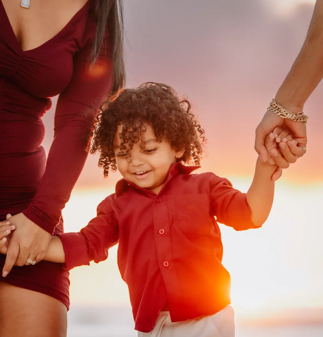 Young boy holding his parents' hands at sunset in Grand Cayman