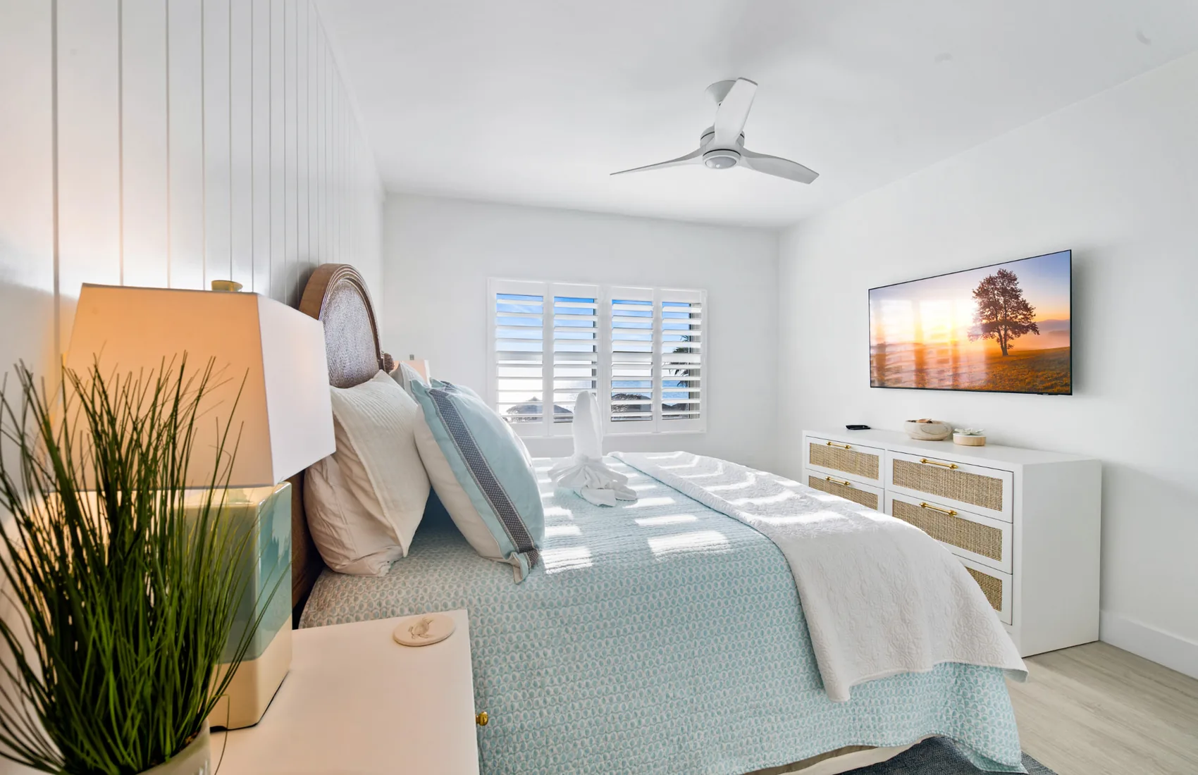 Coastal bedroom with a wicker headboard and shutters framing the sea in Grand Cayman