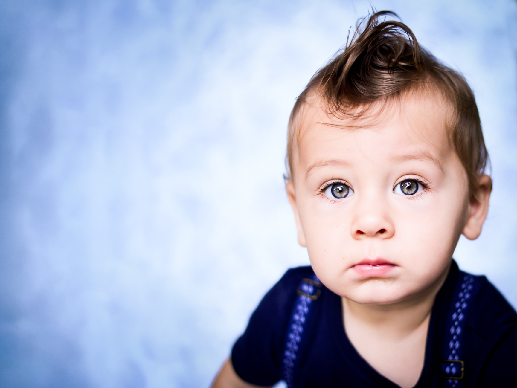 Wide-eyed toddler boy in braces against a soft blue backdrop