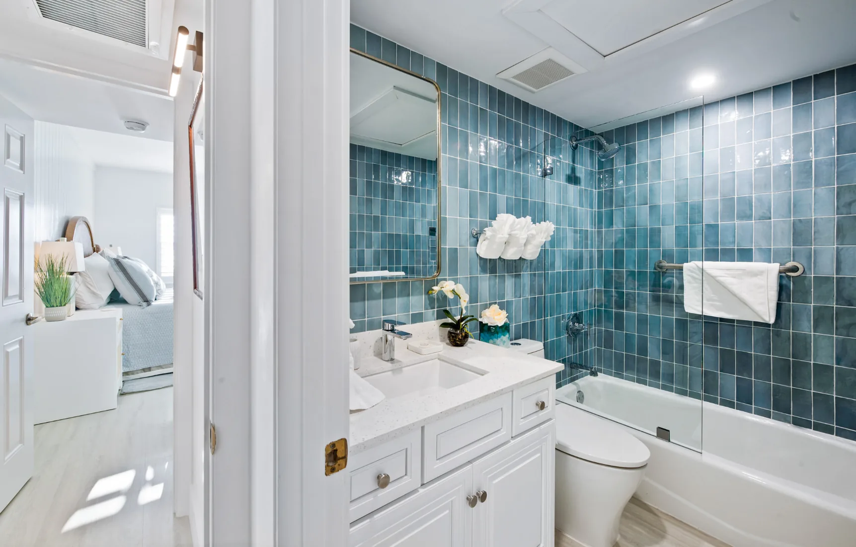 Bathroom with a blue tiled bathtub wall and a round brass mirror in Grand Cayman