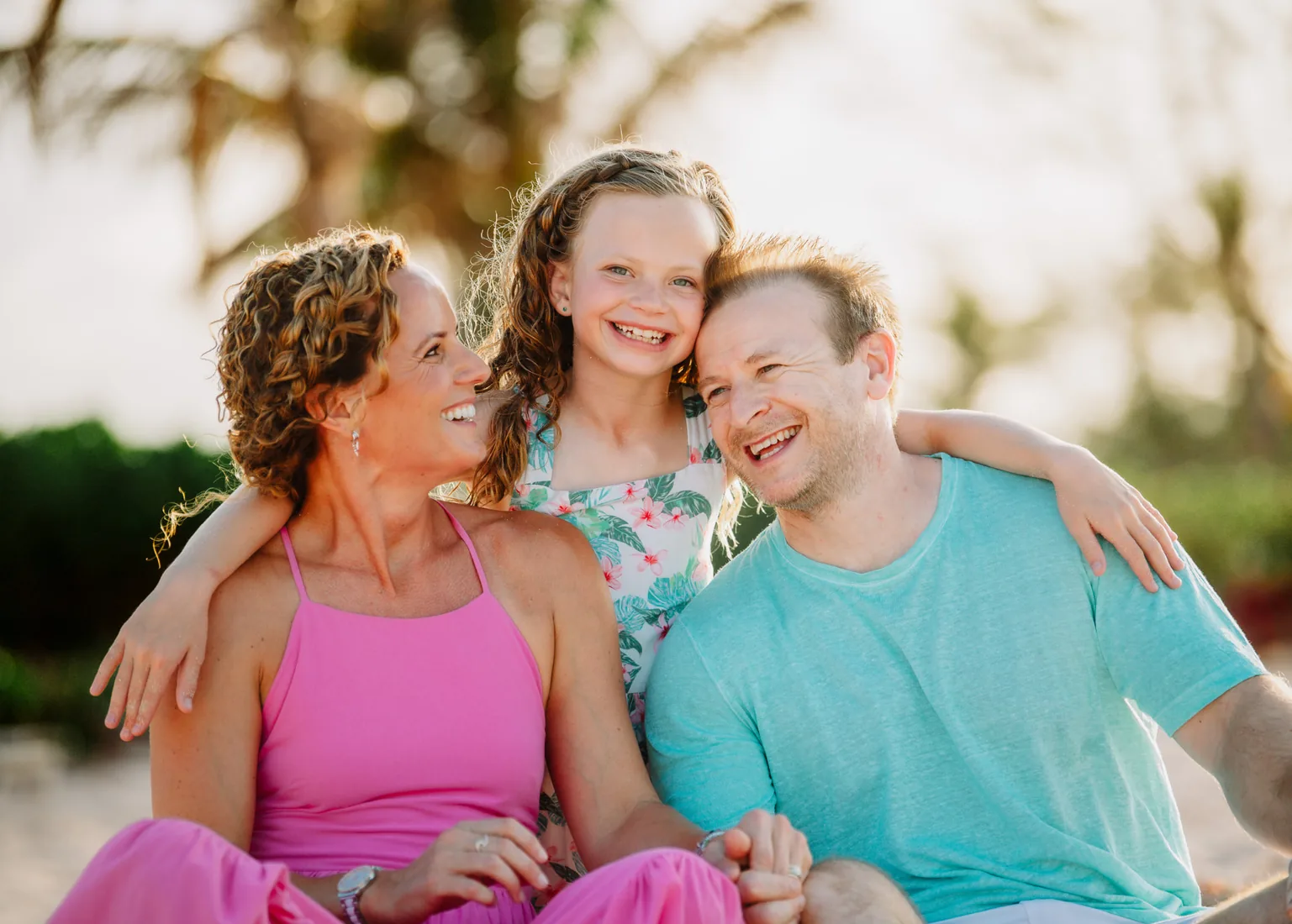 Parents sitting with their daughter on the sand, laughing and holding each other close