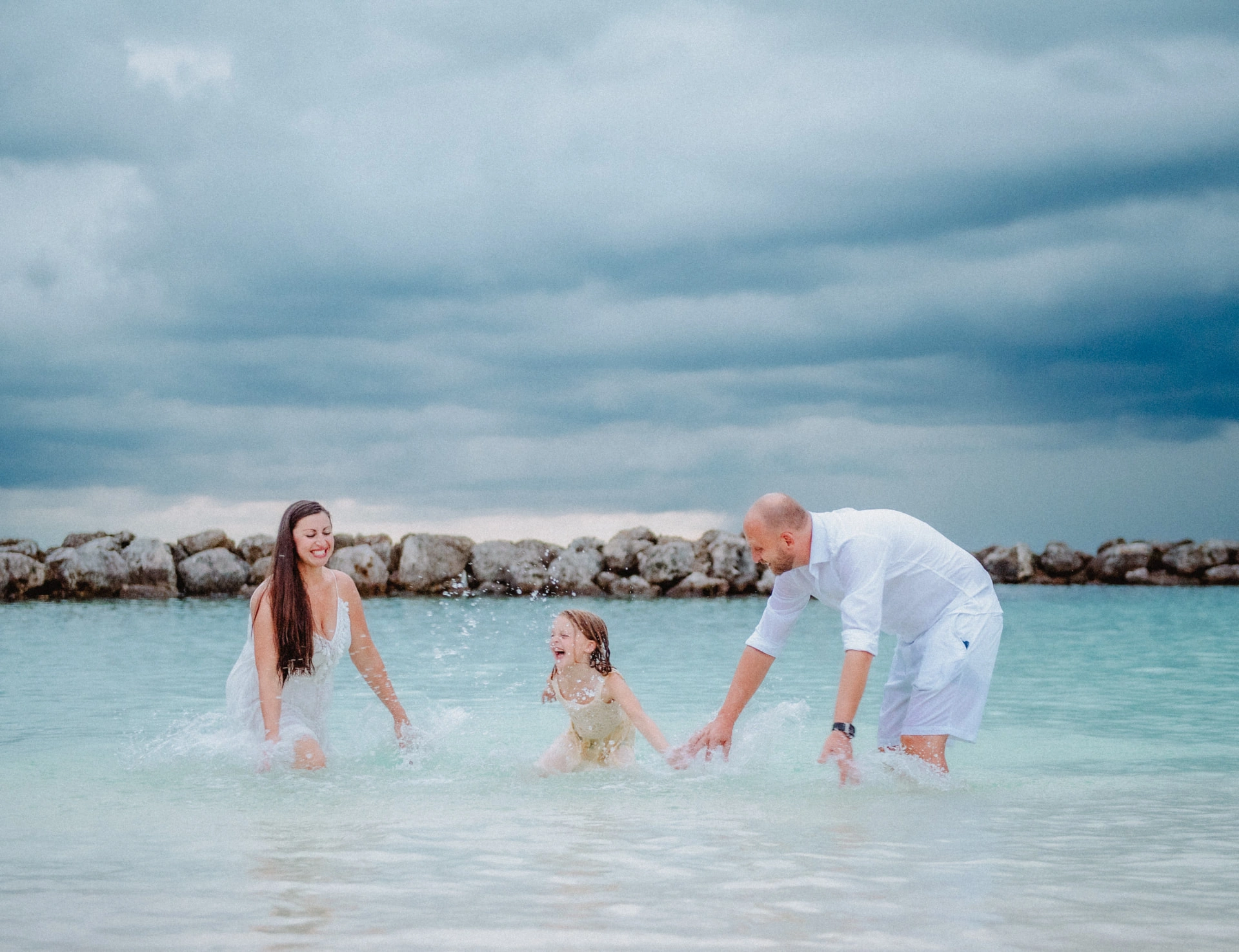 Family laughing and splashing together in the shallows beneath a stormy Cayman sky