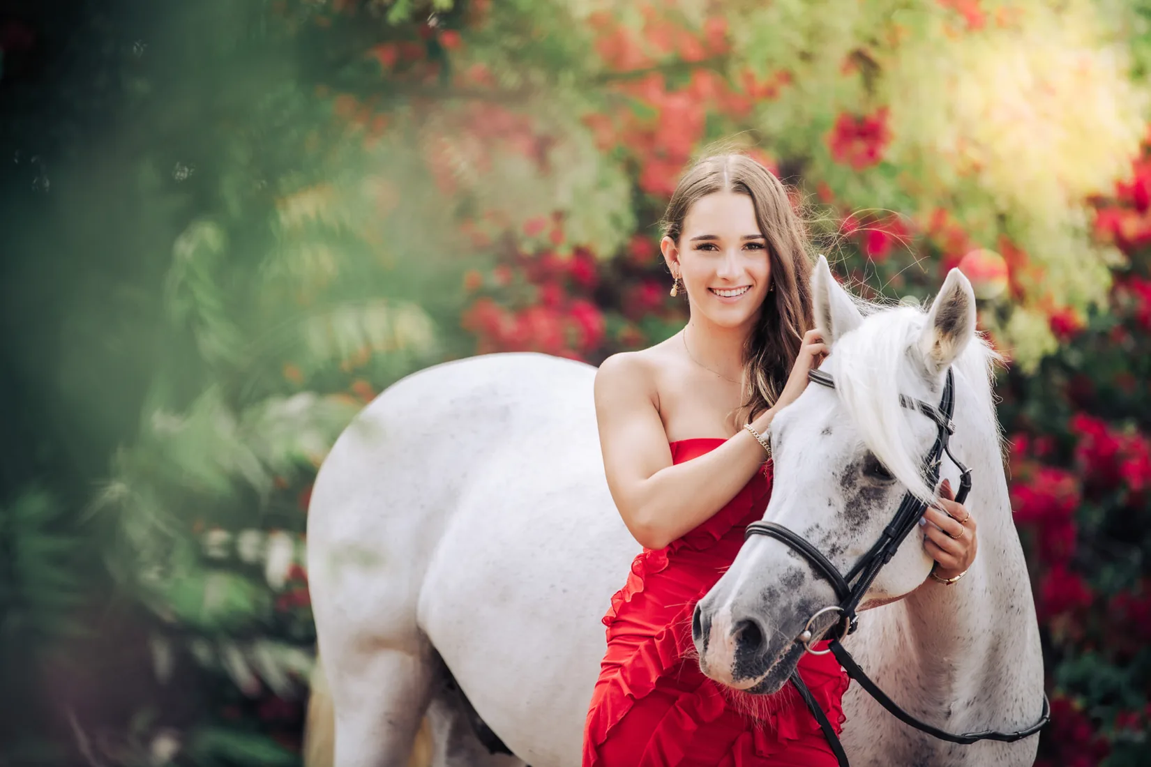 Woman in a red dress standing with her white horse among the flowers in Grand Cayman