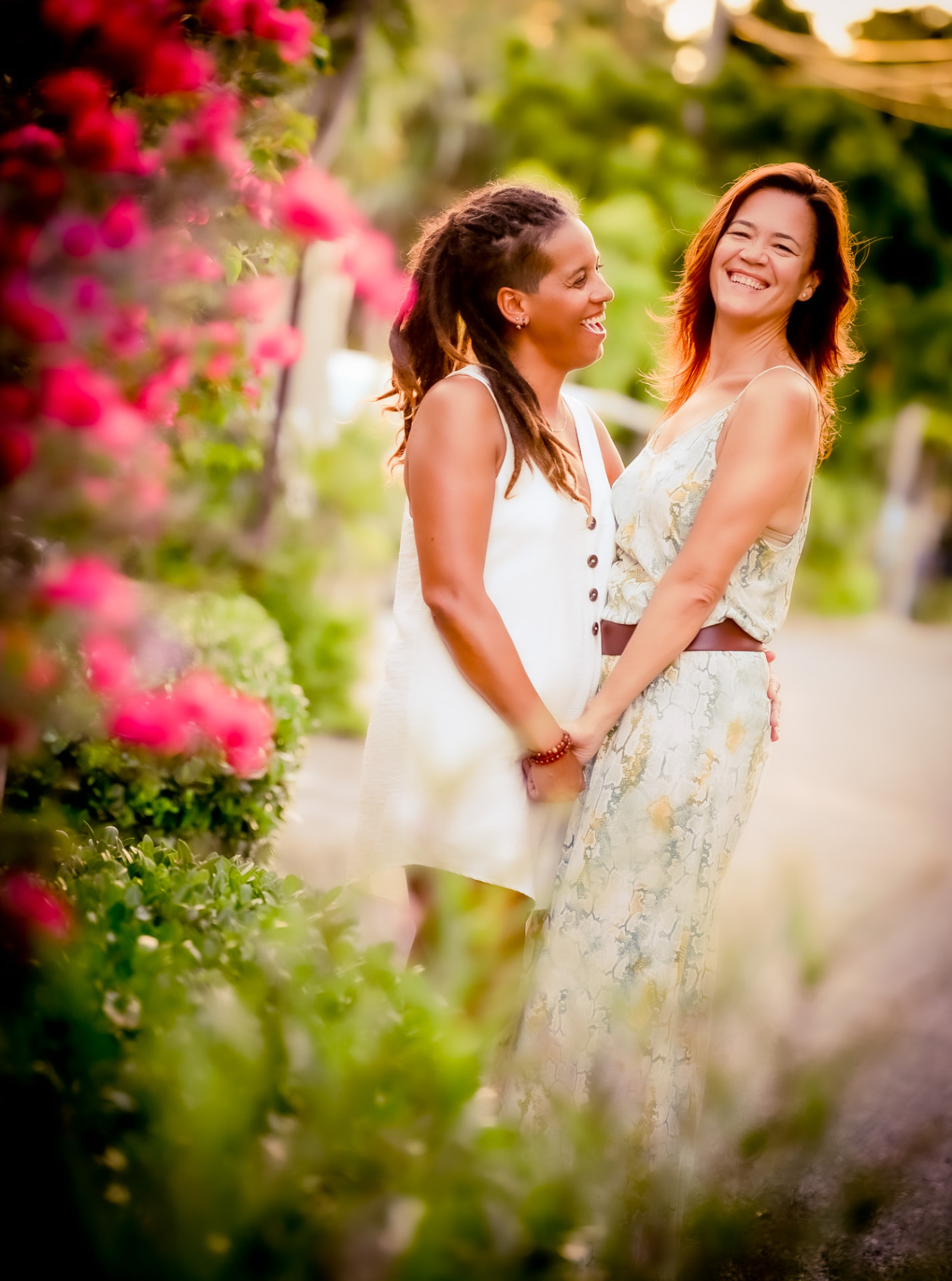 Two women laughing and holding hands among tropical blossoms