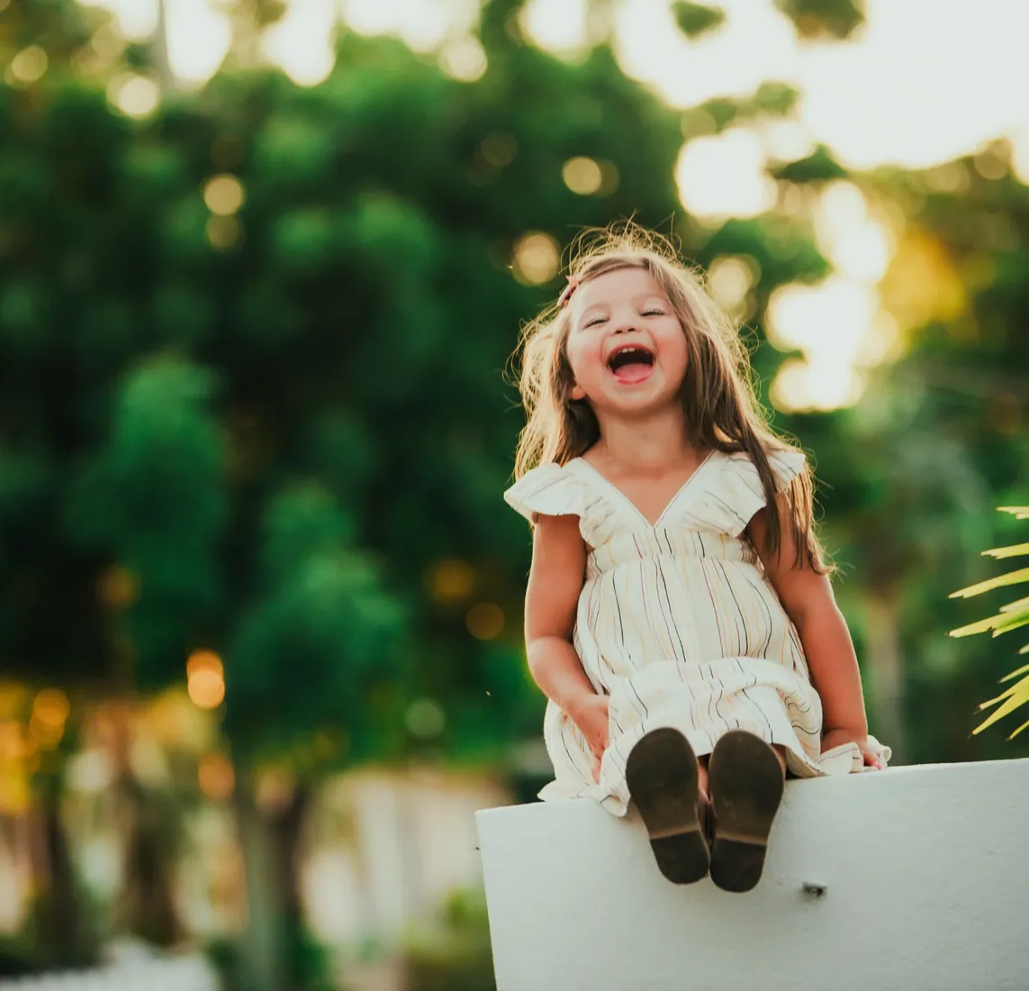 Laughing girl seated on a white wall beneath trees in Grand Cayman