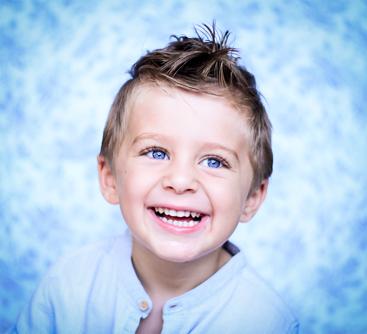 Laughing blue-eyed boy against a soft blue backdrop