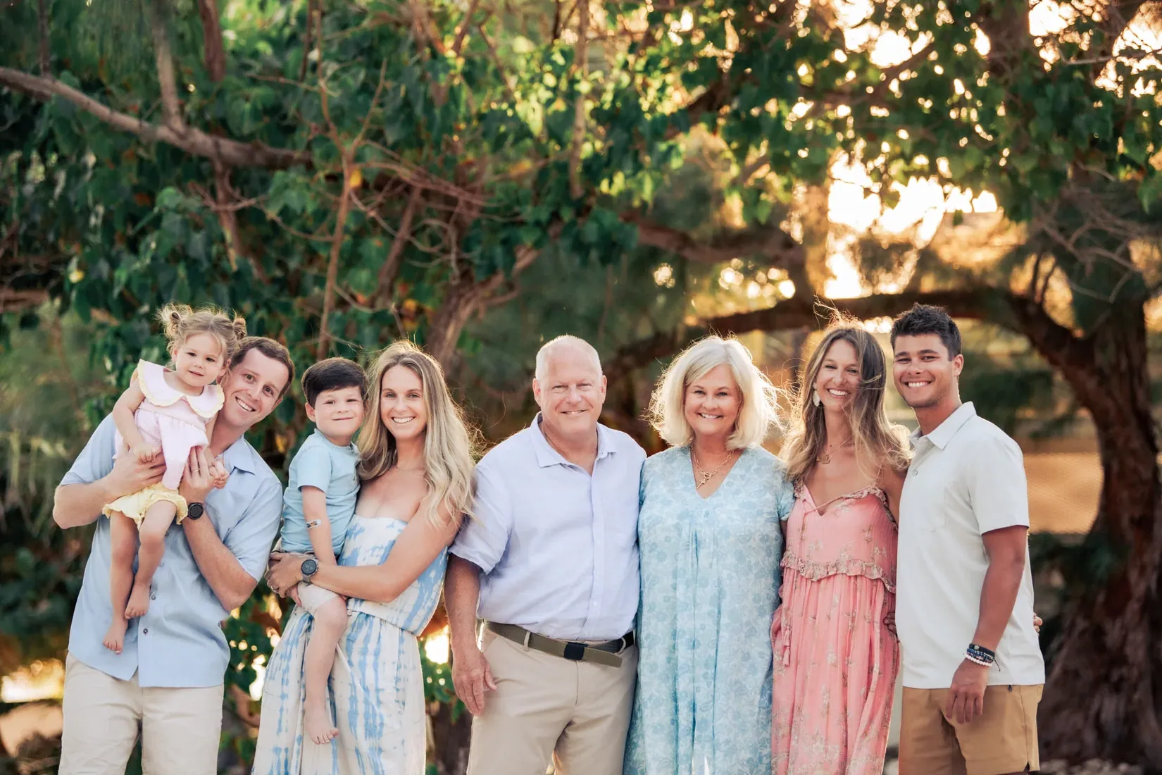 Extended family smiling together beneath sunlit trees in Grand Cayman