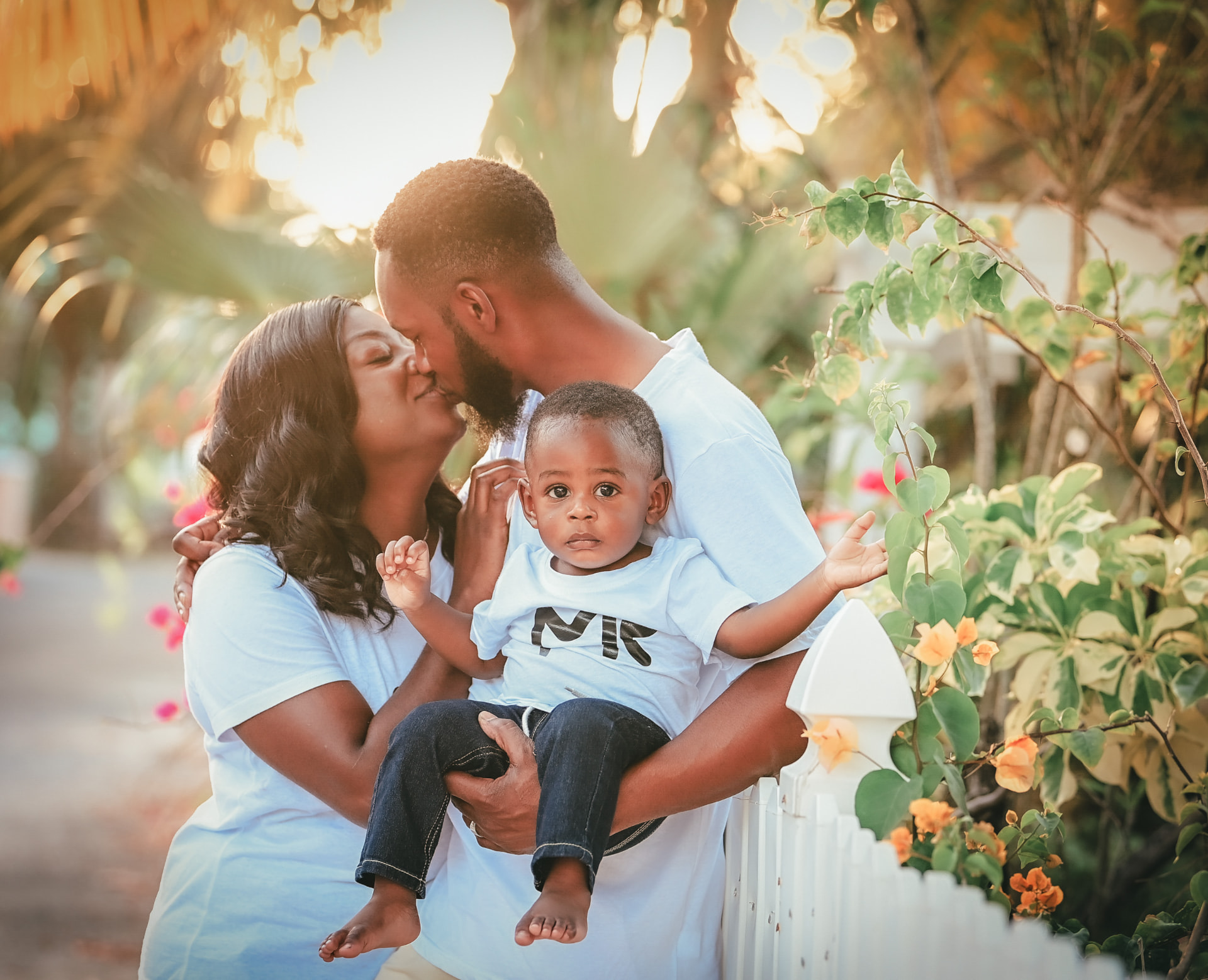 Family in matching light blue outfits sharing a moment with their toddler among tropical greenery