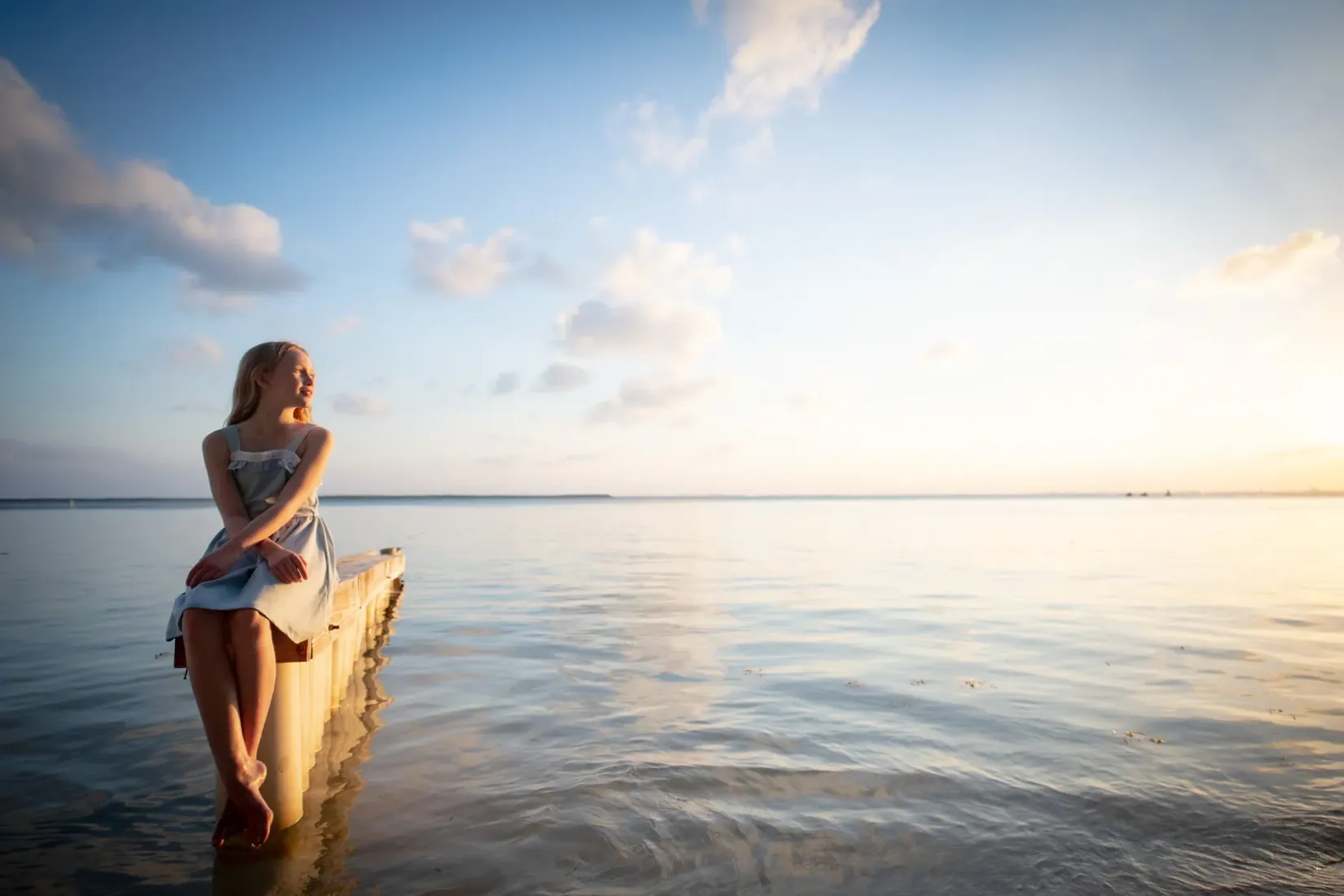 Girl seated on a jetty beside calm water at sunset in Grand Cayman