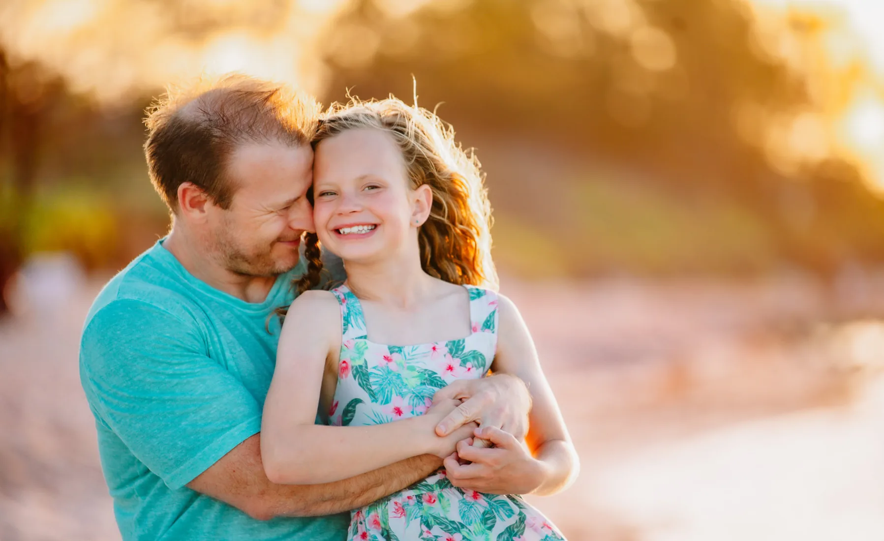 Father hugging his smiling daughter on the beach at golden hour in Grand Cayman