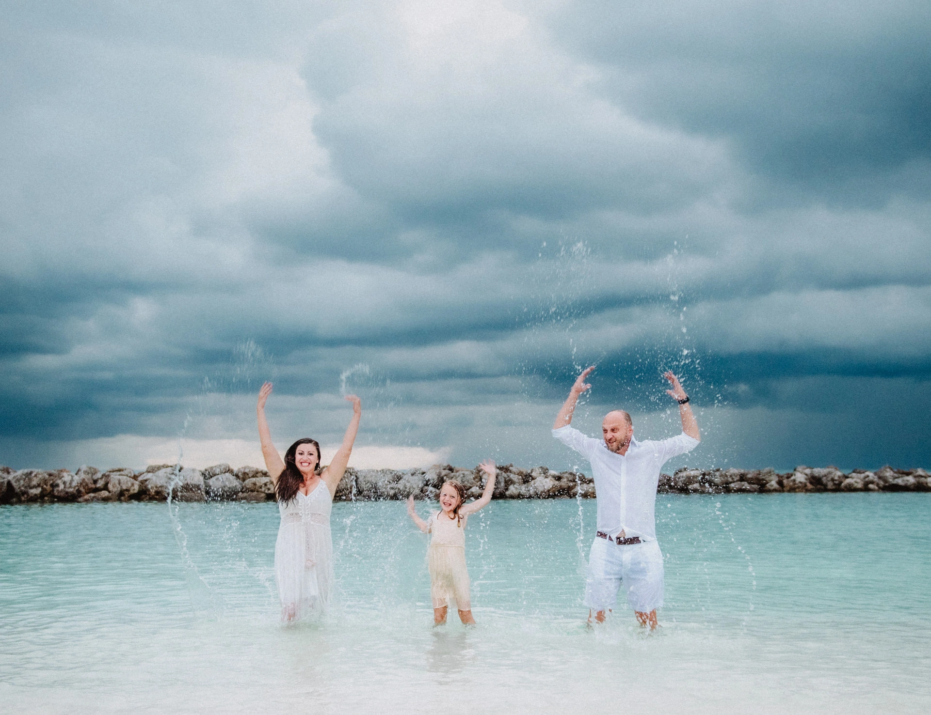 Parents and their daughter splashing in the sea under heavy rain clouds in Grand Cayman