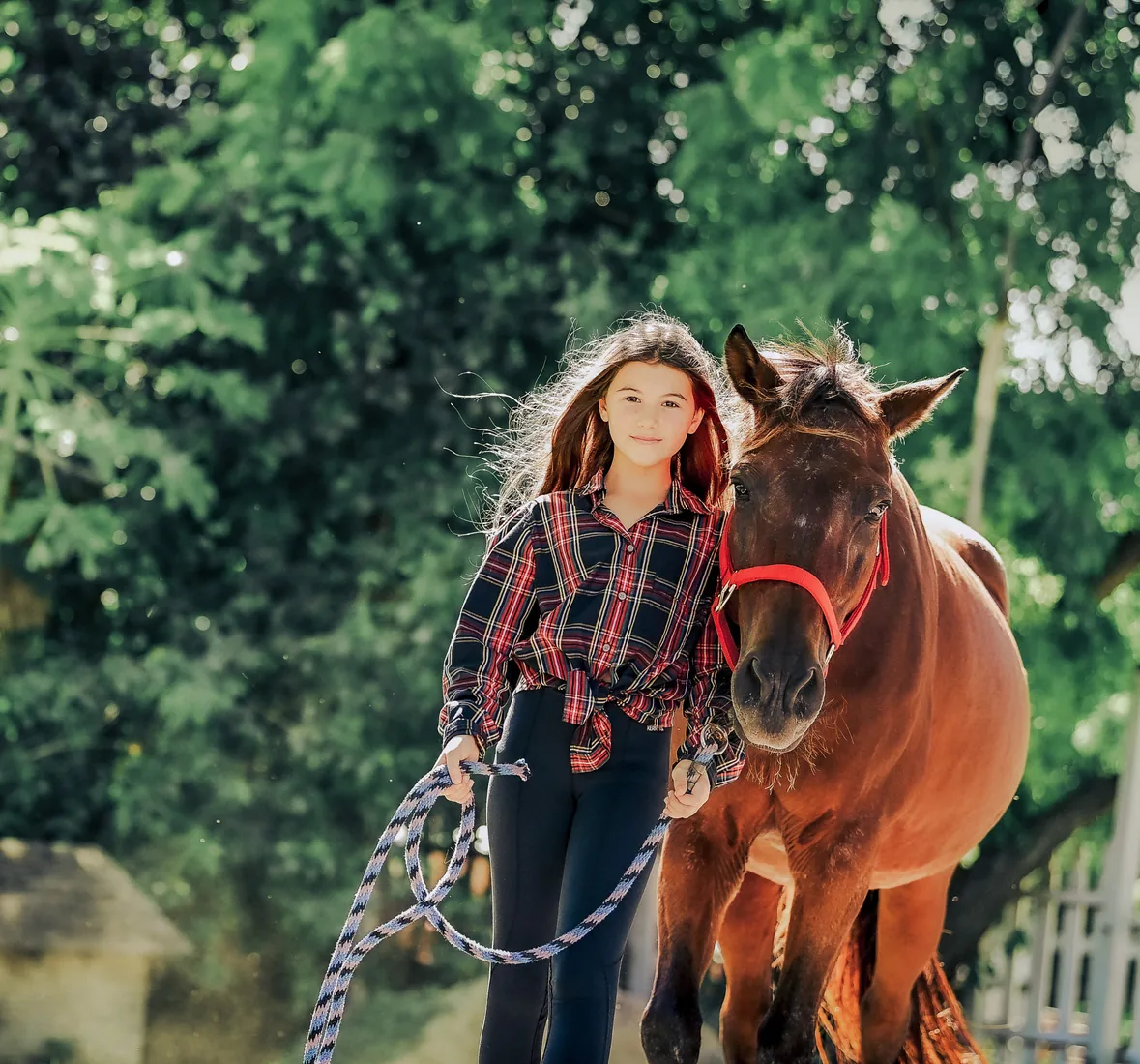 Girl in a plaid shirt standing beside her brown pony in Grand Cayman