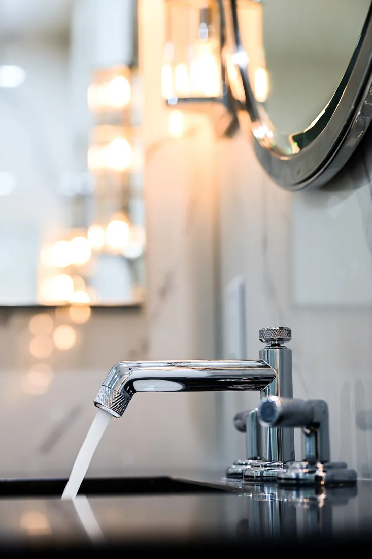 Chrome bathroom tap with water running in warm sconce light in Grand Cayman