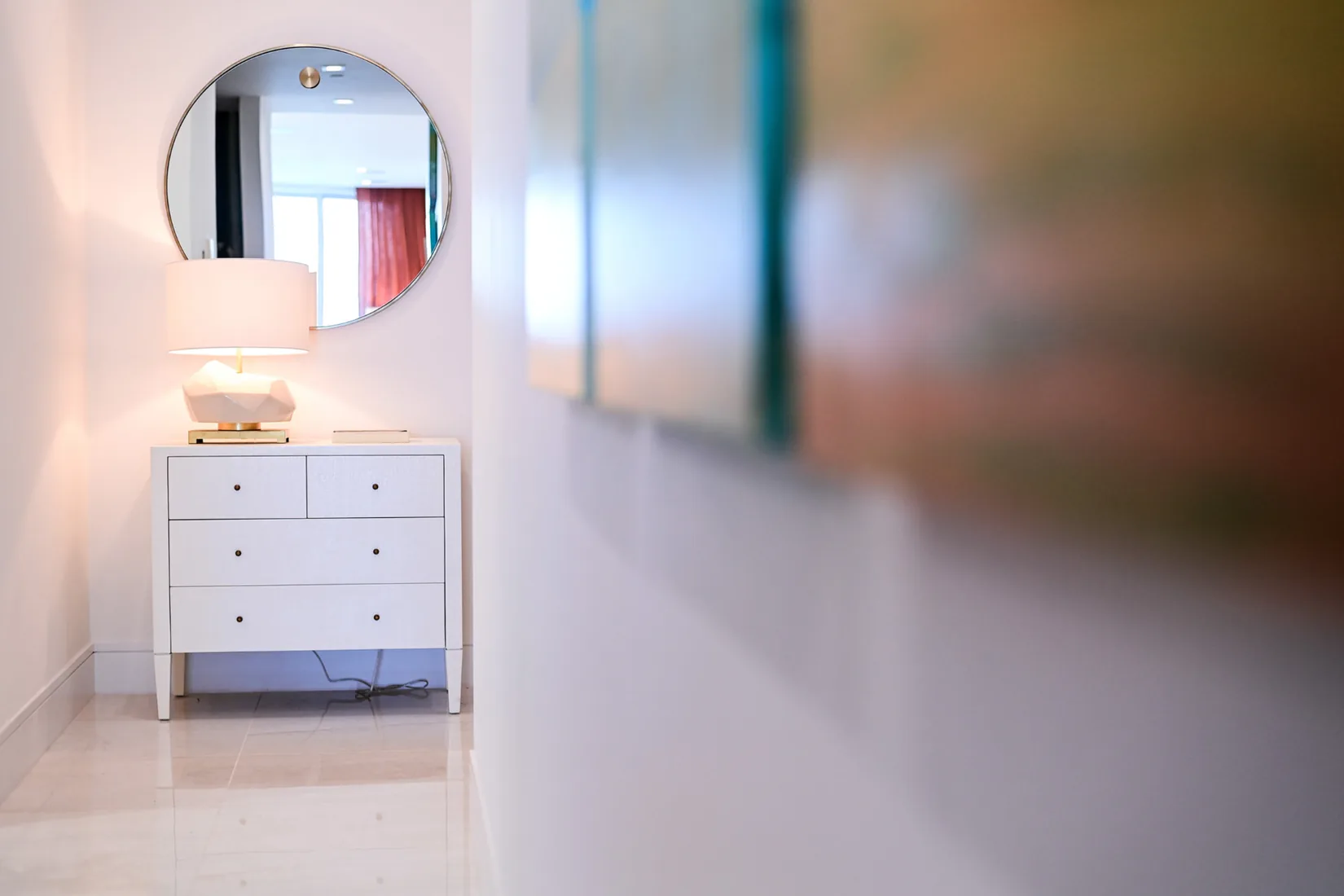 Hallway with a white dresser, geometric lamp and round mirror in Grand Cayman